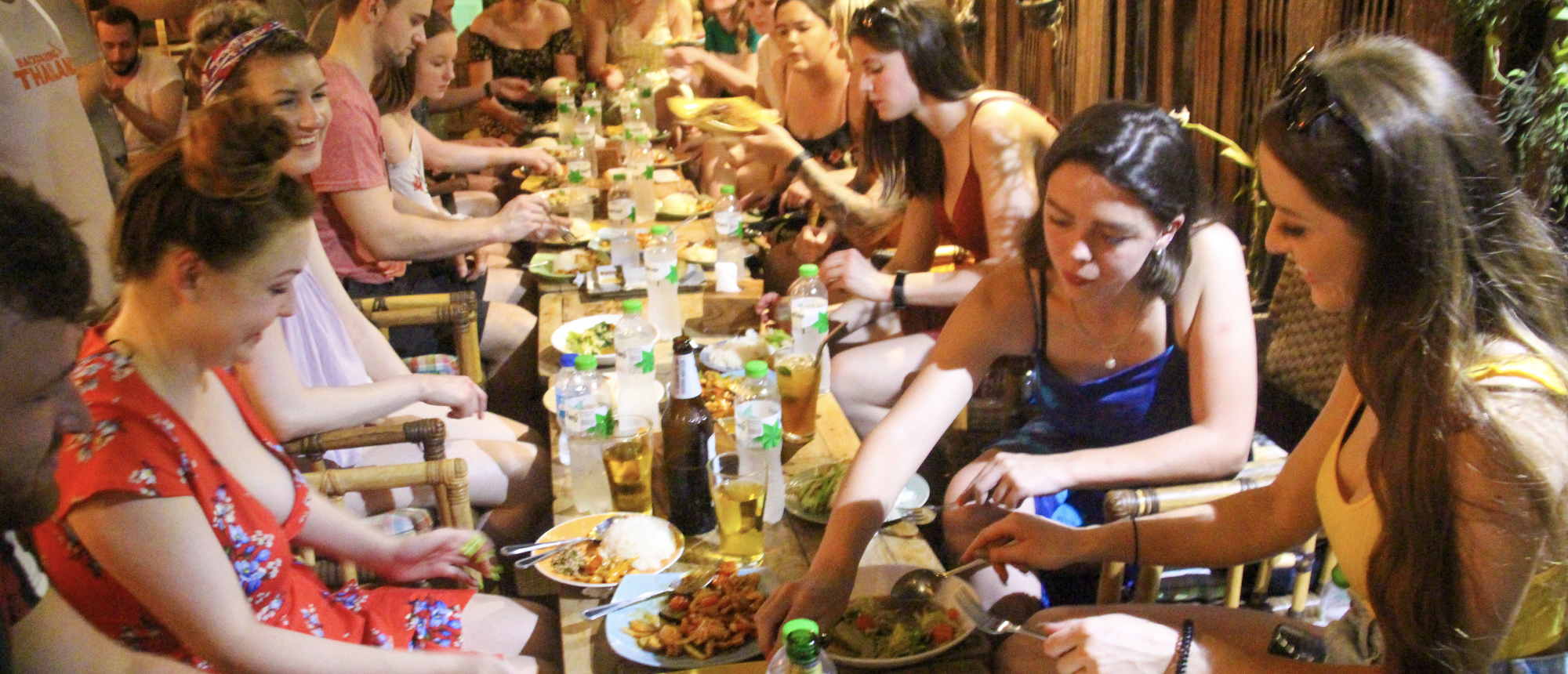 Backpacking group enjoying a shared Thai dinner around a long wooden table