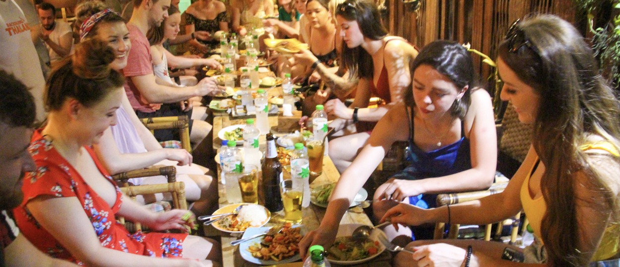 Backpacking group enjoying a shared Thai dinner around a long wooden table