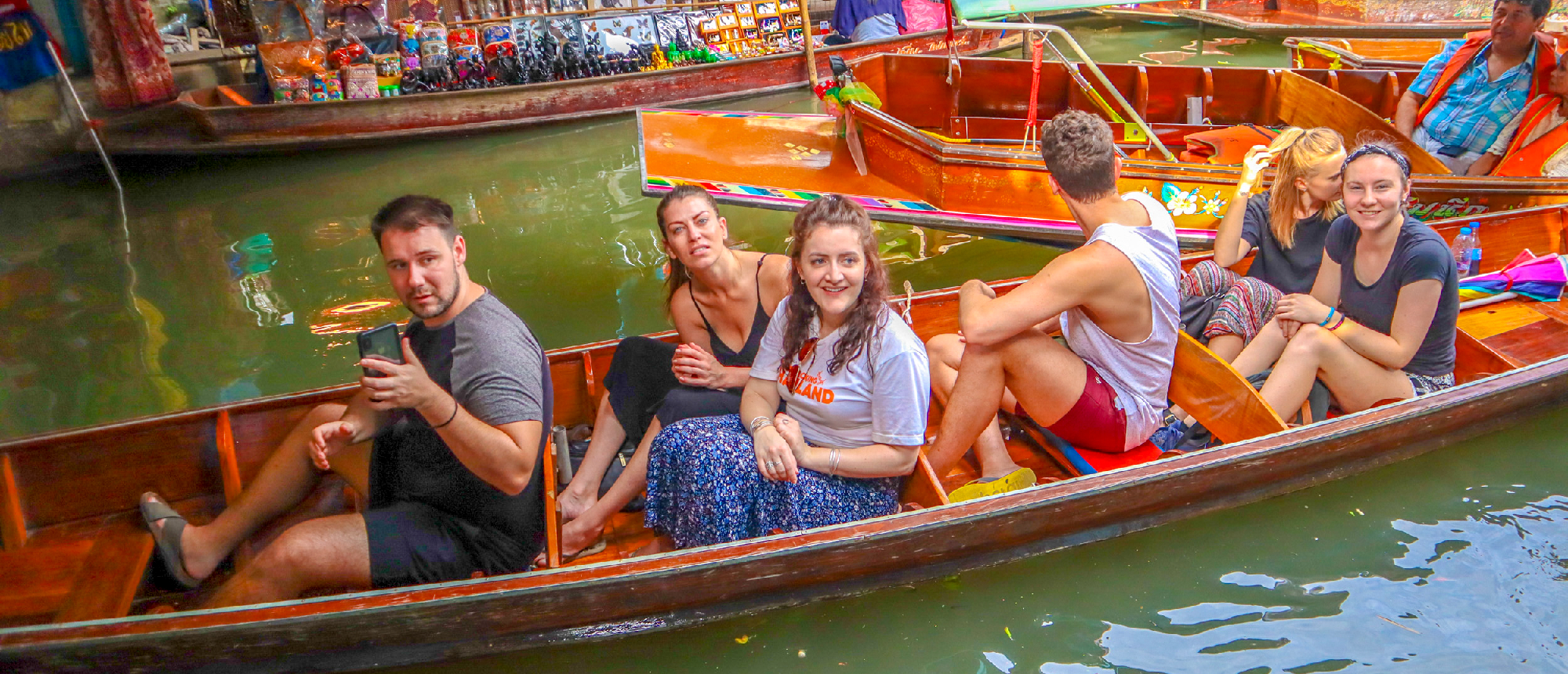 Backpacking group having a fun water fight on a long-tail boat at the floating market