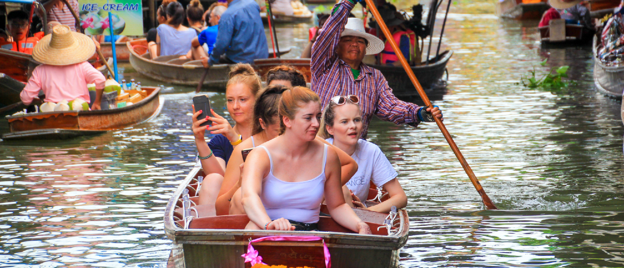 Backpacking group paddling a wooden boat through the Amphawa Floating Market