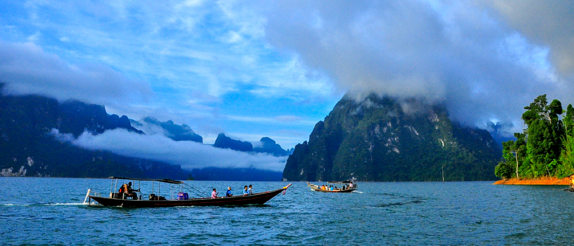 Long-tail boat gliding across Cheow Lan Lake with misty limestone mountains in the background
