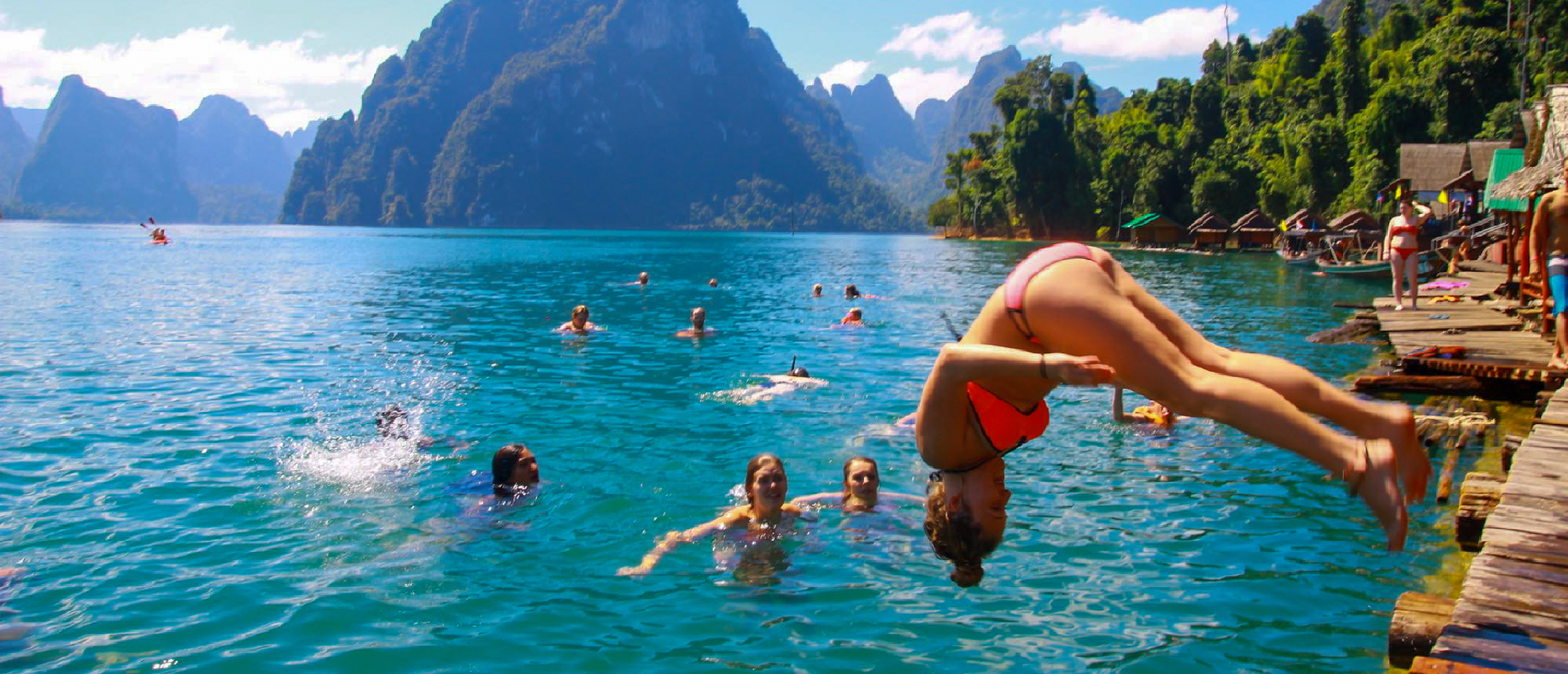 Backpacker diving into the turquoise waters of Cheow Lan Lake from a floating platform while friends watch