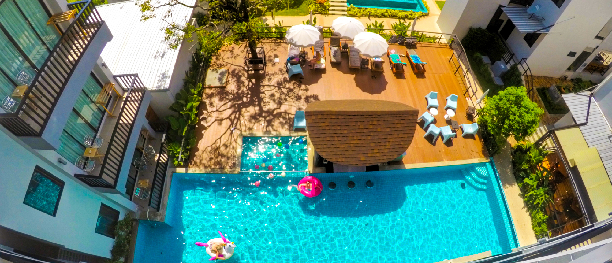 Aerial view of a resort swimming pool with lounge chairs and lush palm trees in Ao Nang