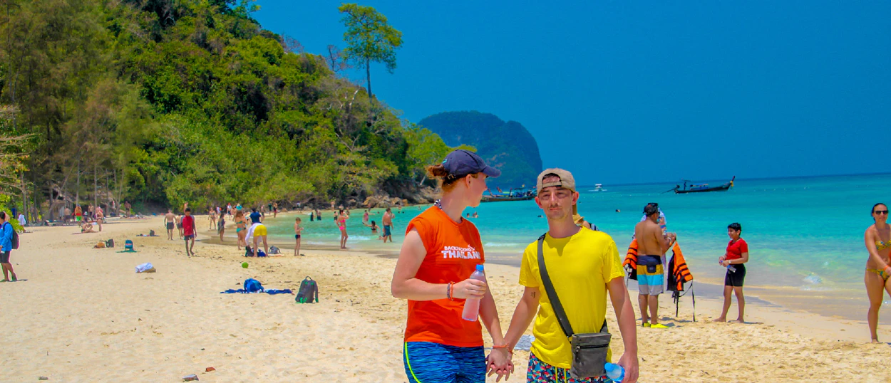 A young couple walks hand-in-hand on a sunny beach in Krabi, Thailand.