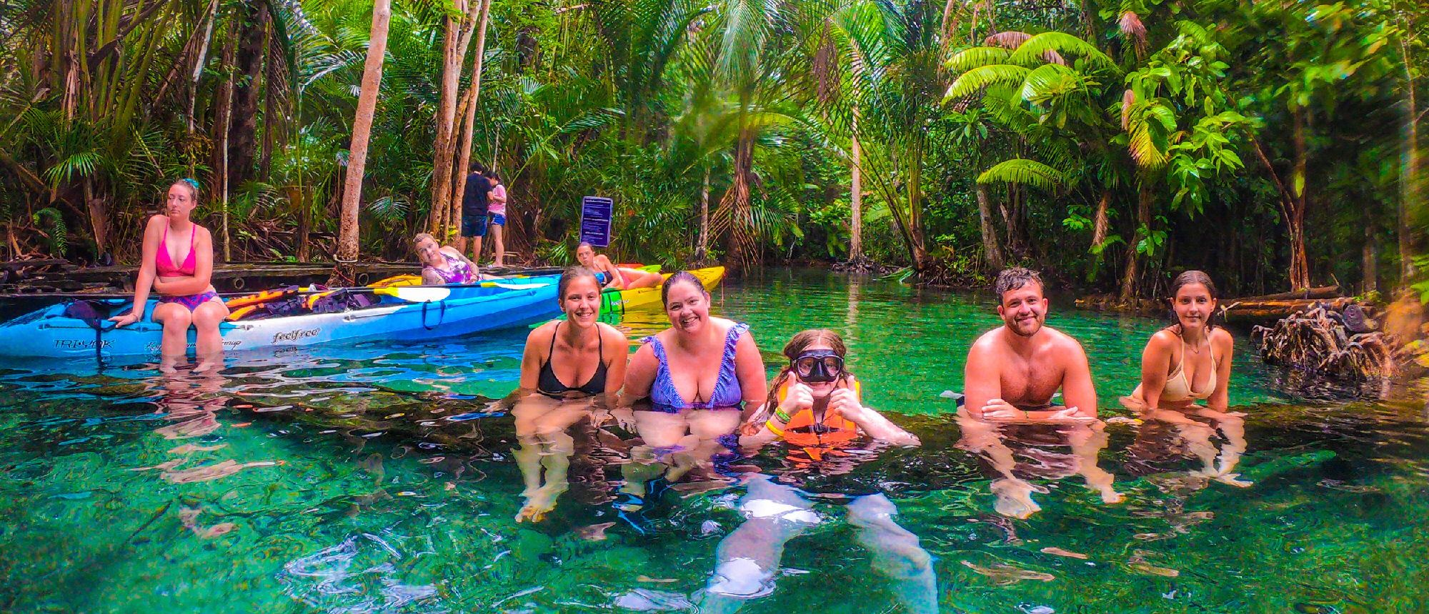 Backpacking group swimming and relaxing in an emerald-green river surrounded by lush jungle during a mangrove kayak adventure
