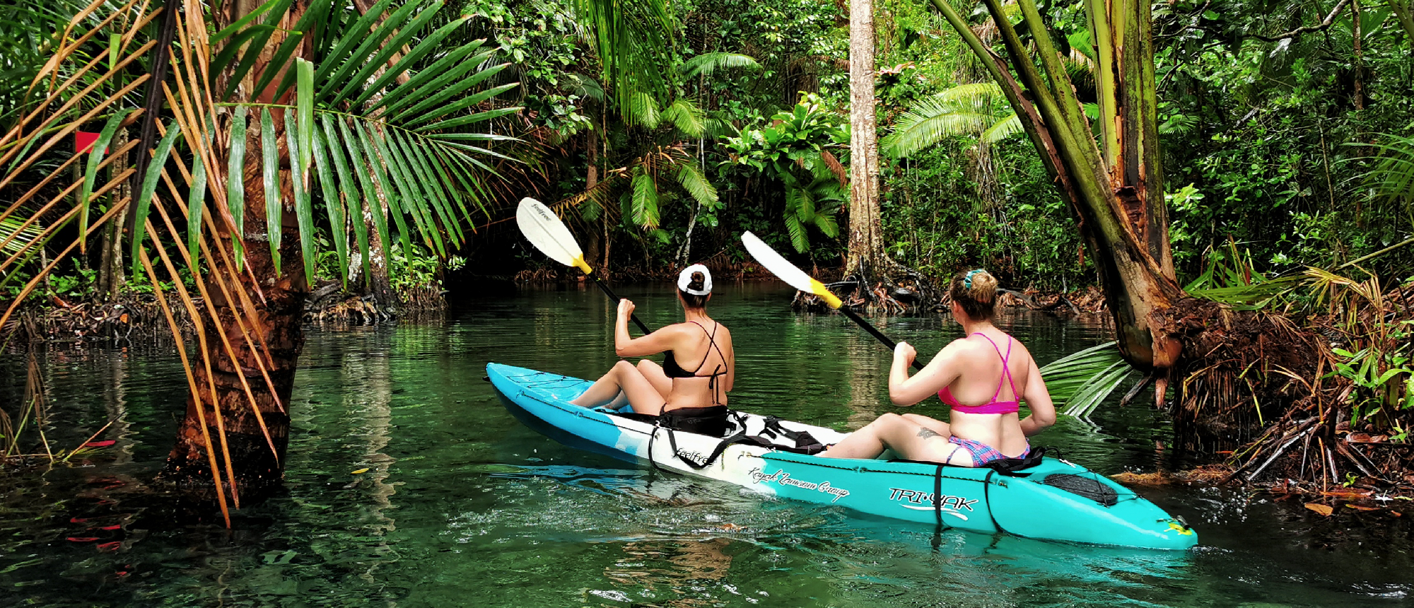 Backpacking couple paddling a kayak through a calm mangrove canal surrounded by lush trees