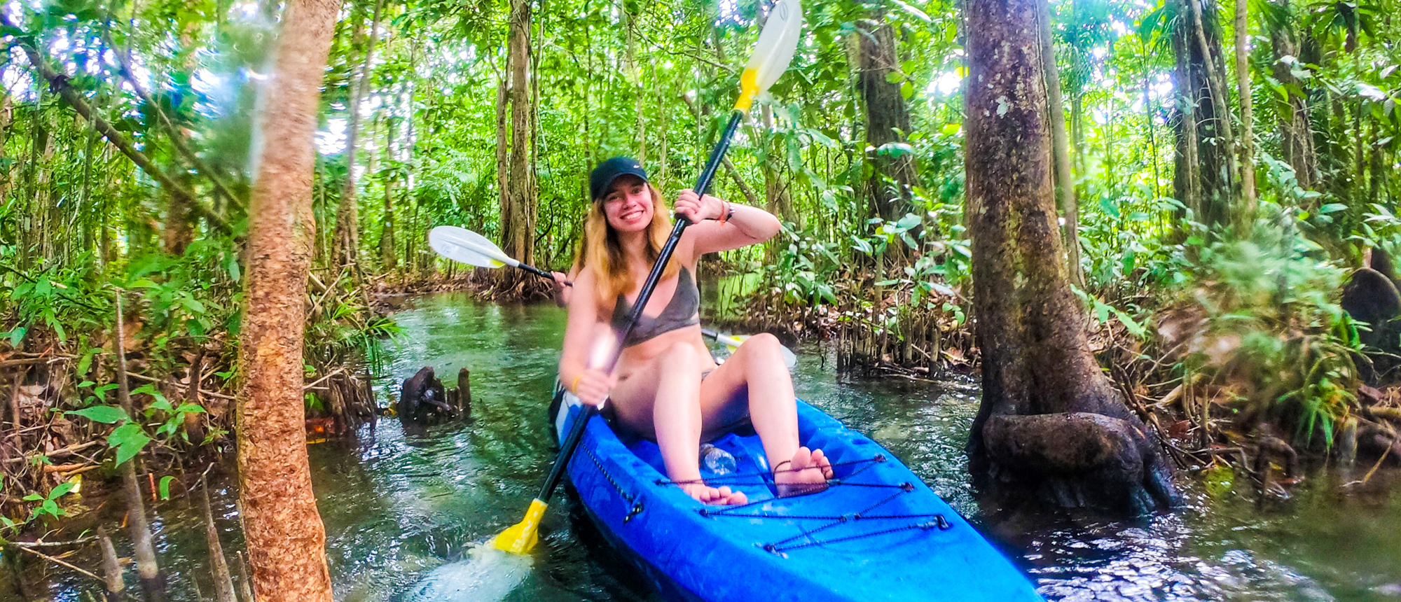 Backpacking couple relaxing in a blue kayak in a mangrove forest, taking a break on the river