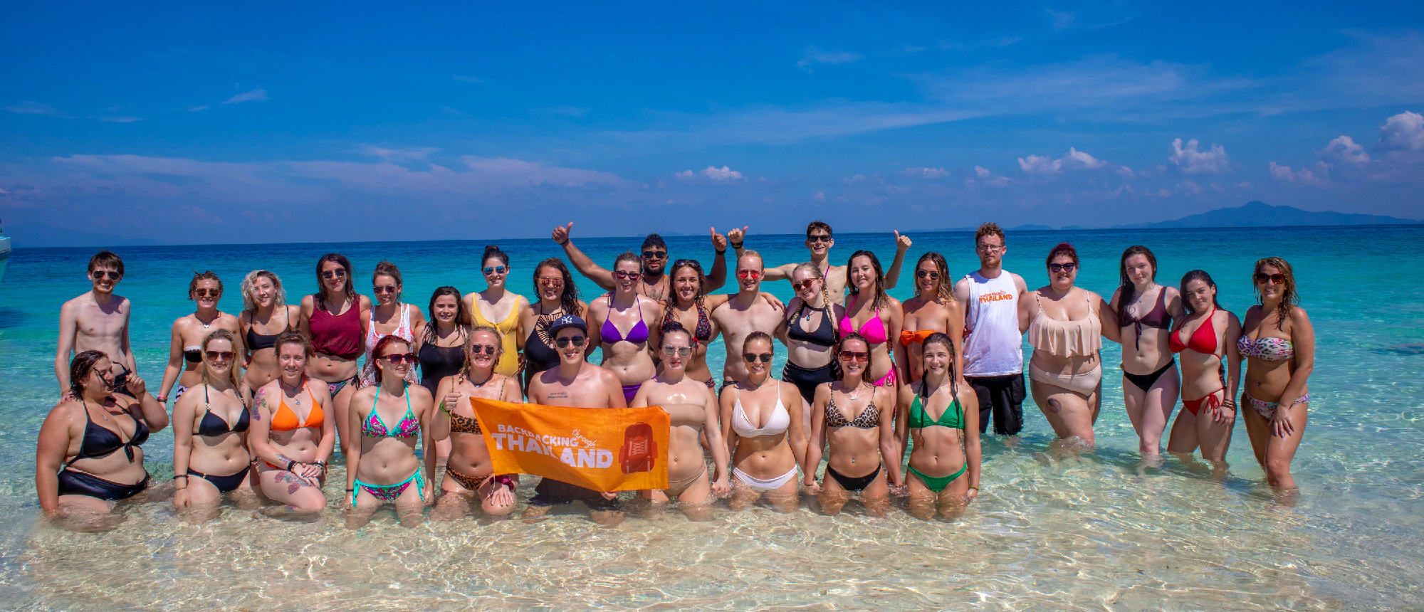 Backpacking group posing together on a white sandy beach with turquoise water and limestone cliffs