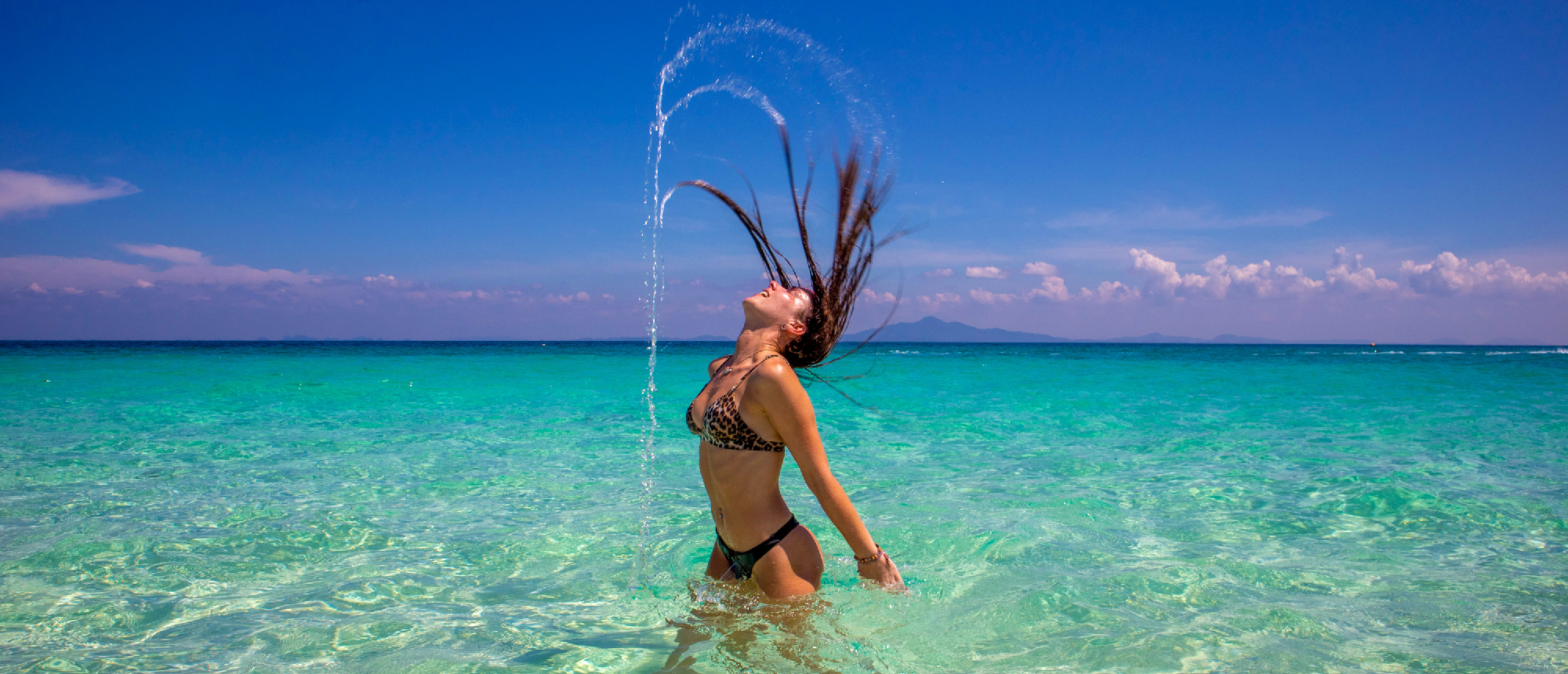 Traveller swinging a rope while standing in shallow turquoise water on a white sandy beach