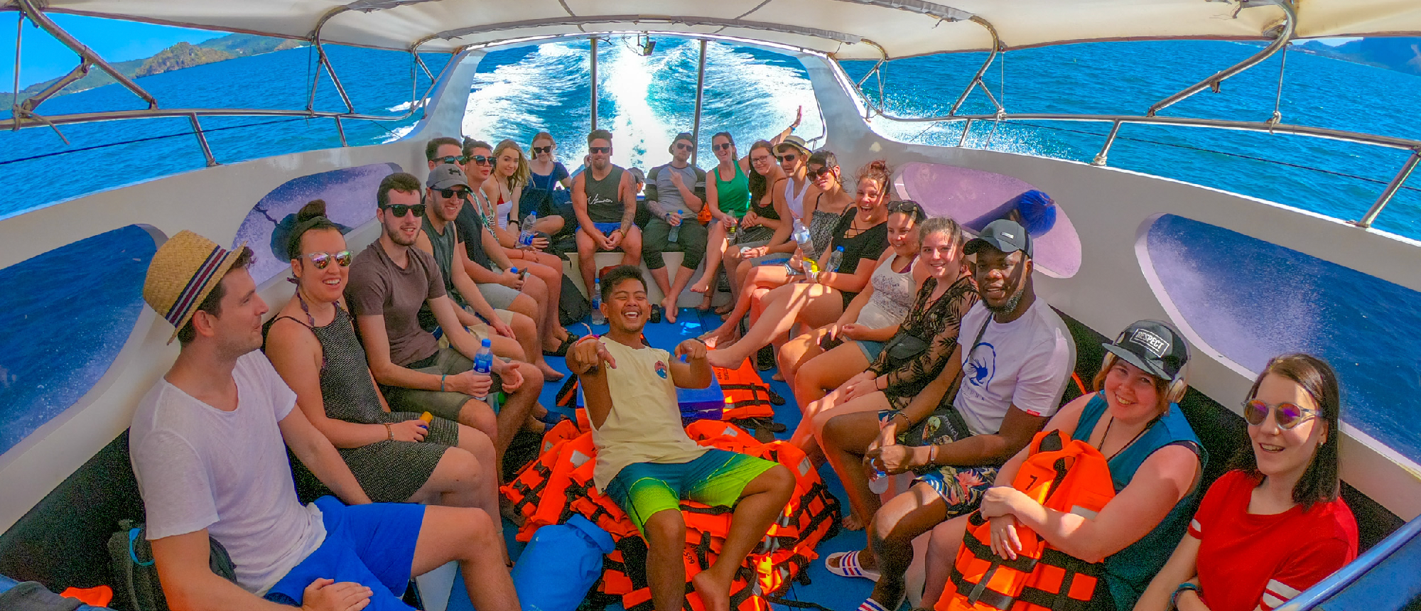 Backpacking group wearing life jackets seated inside a speedboat ready for island hopping