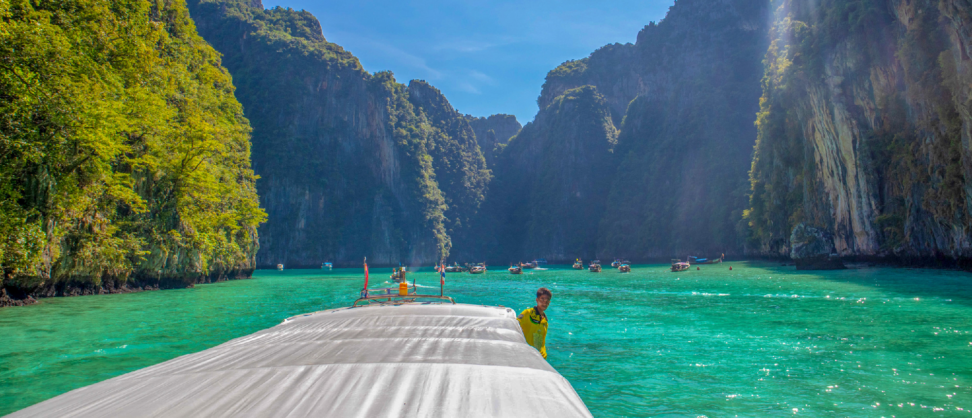 View of turquoise lagoon and towering limestone cliffs from a floating dockBackpacking couple sitting on the bow of a speedboat heading toward limestone islands in turquoise sea