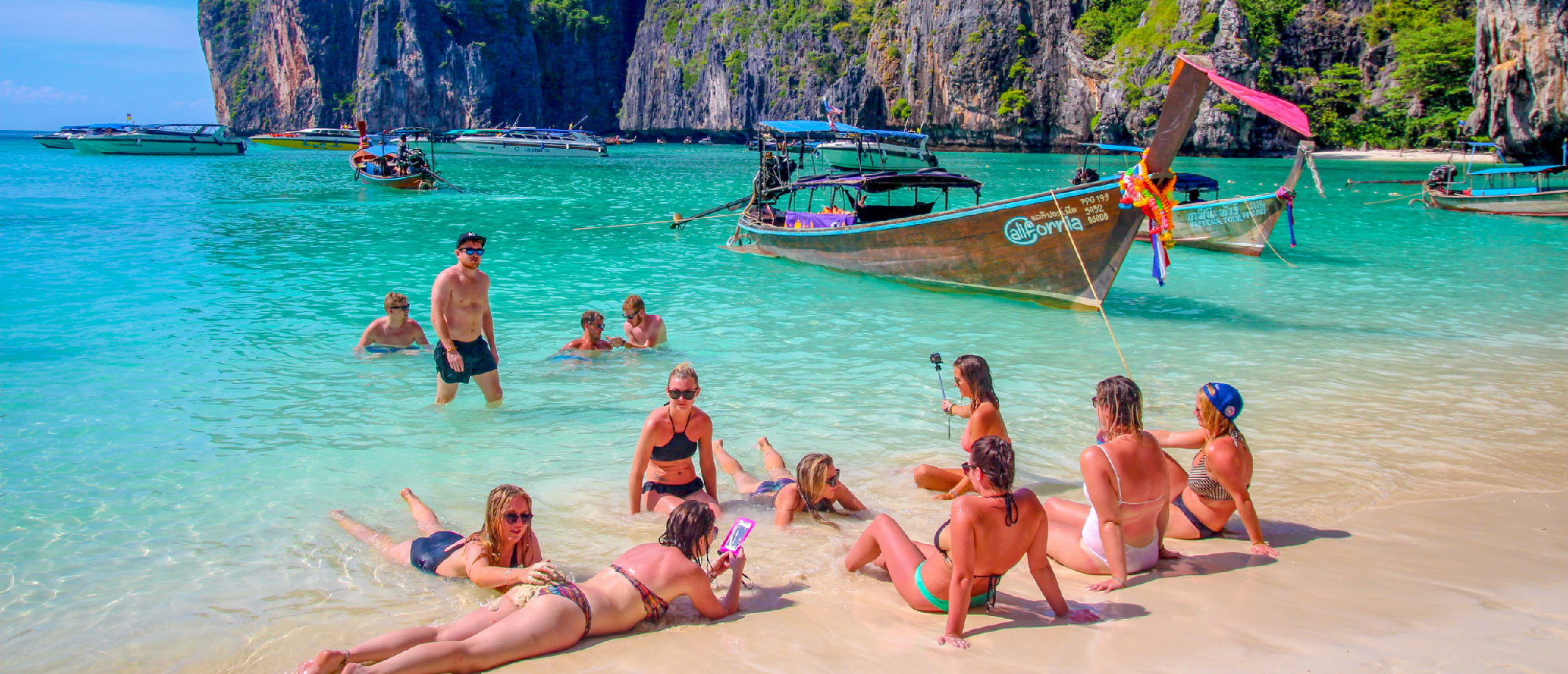 Backpacking group relaxing on a sandy beach on Koh Phi Phi with turquoise water and limestone cliffs