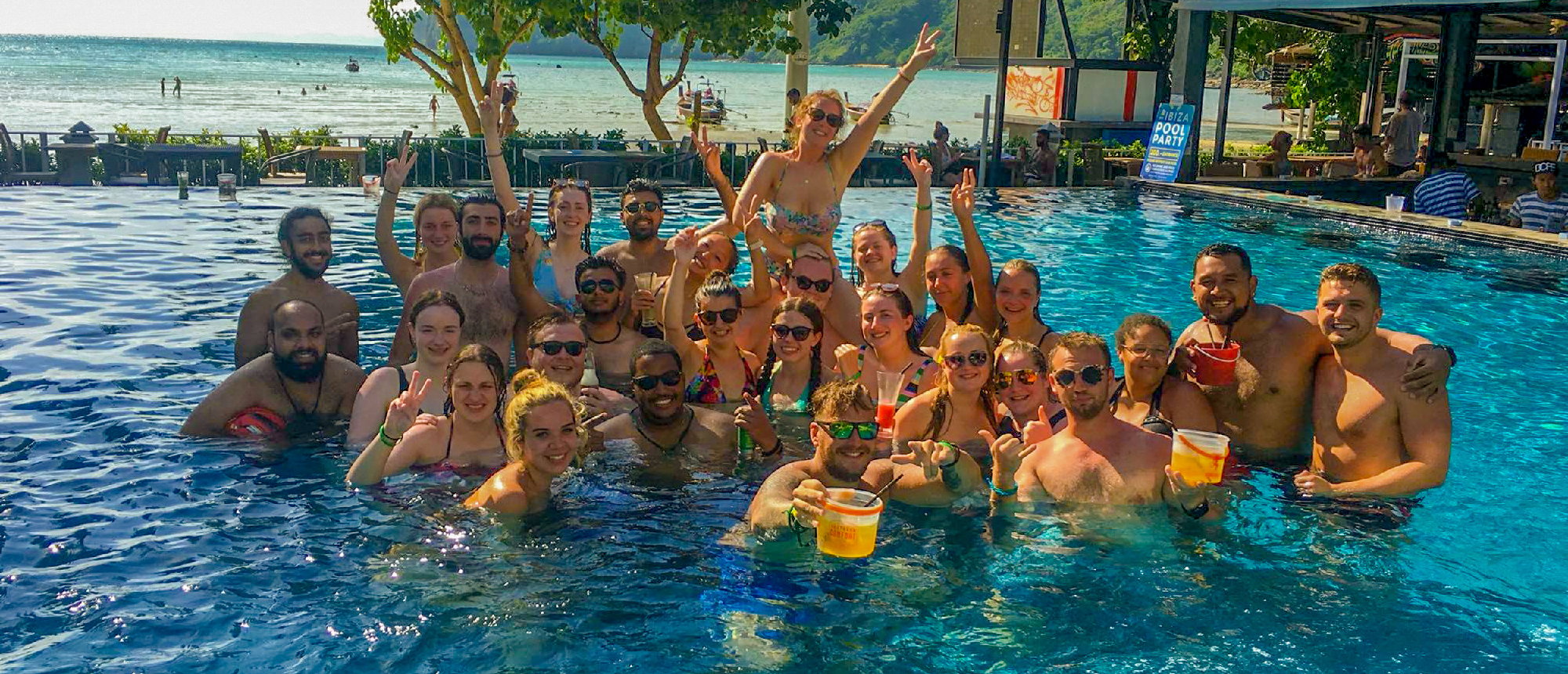 Backpacking group gathered in a swimming pool raising their hands during a pool party