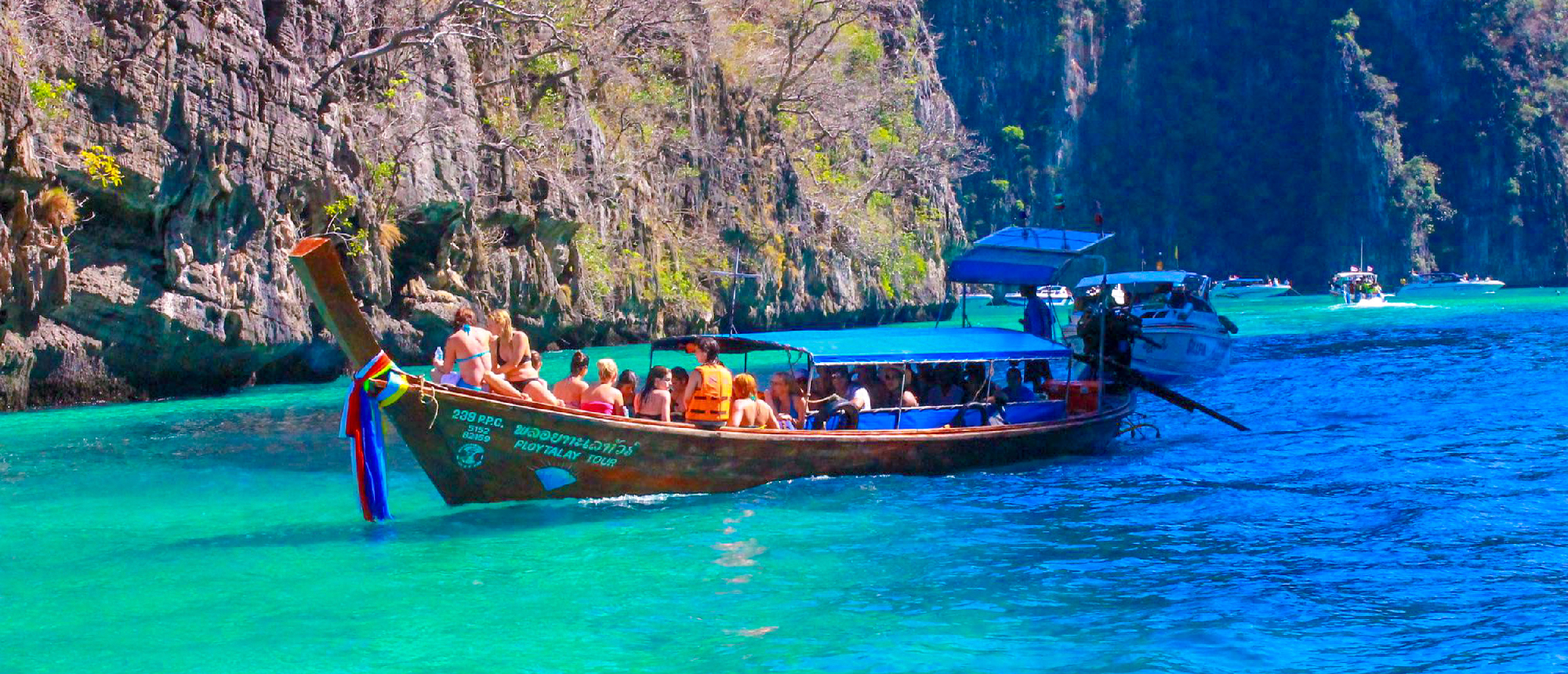 Long-tail boat anchored in turquoise waters with towering limestone cliffs at Railay BeachColorful long-tail boats lined up on the sandy beach at Railay Beach with limestone cliffs in the backgroundColorful long-tail boats lined up on the sandy beach at Railay Beach with limestone cliffs in the backgroundColorful long-tail boats lined up on the sandy beach at Railay Beach with limestone cliffs in the background