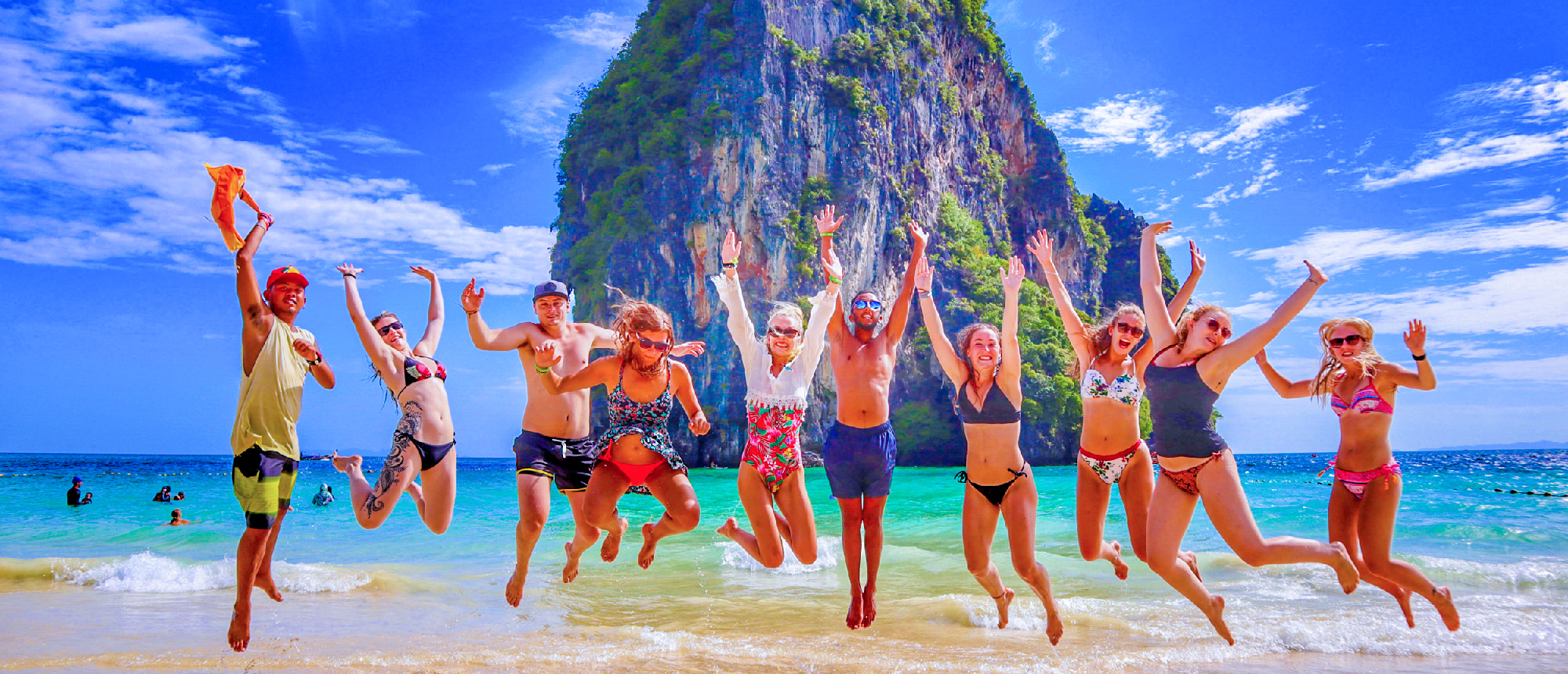 Backpacking group jumping in the air on Railay Beach with turquoise water and limestone cliffs in the background