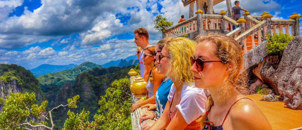 Backpacking group taking a selfie at a hilltop viewpoint with a monkey and panoramic views of the valley