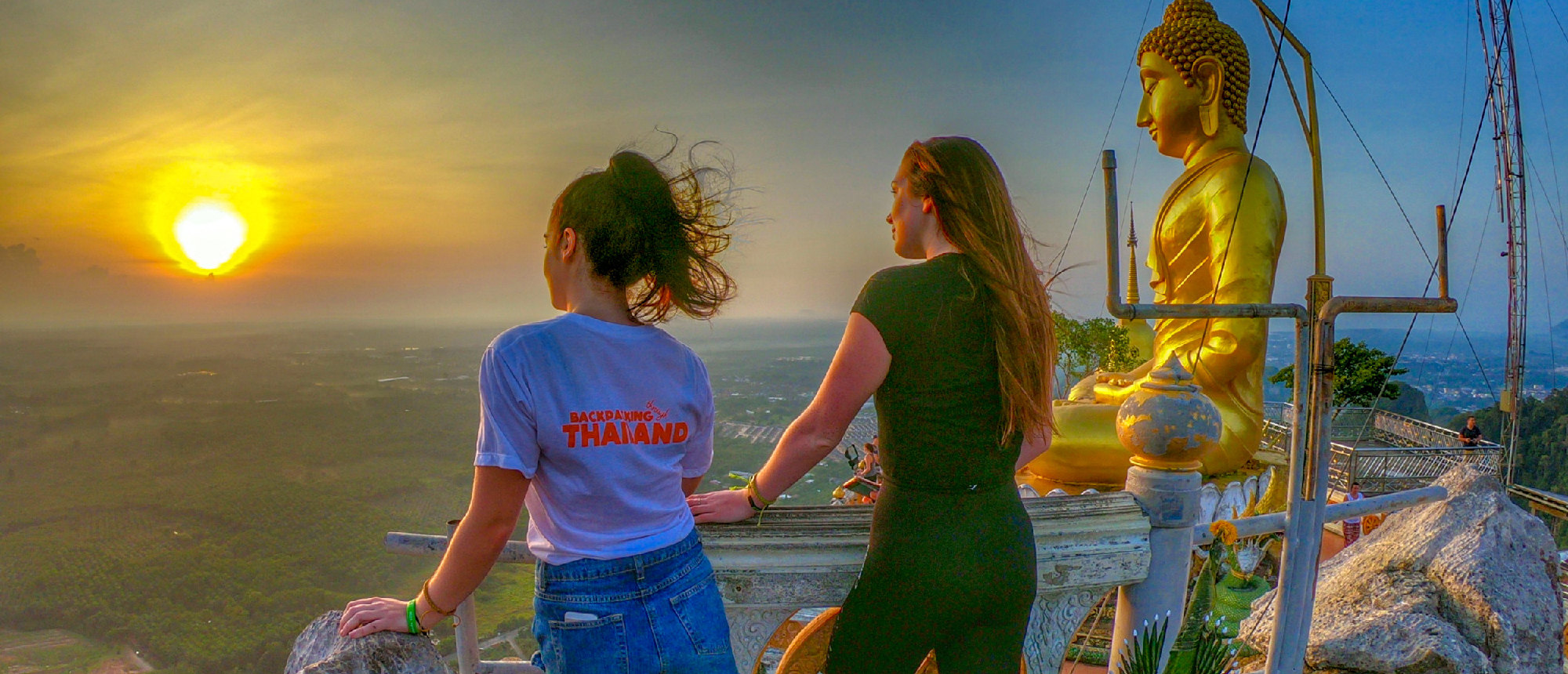 Backpacking group watching the sunset from a long-tail boat on calm water with limestone cliffs in the background