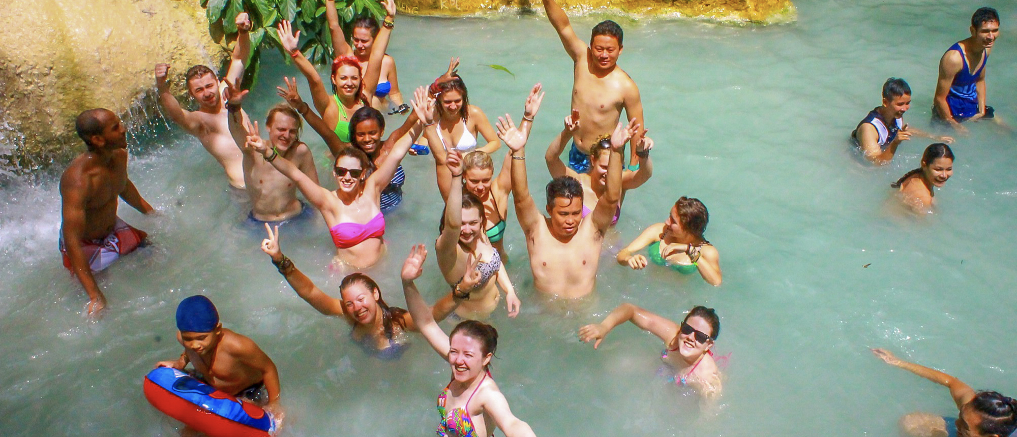 Backpacking group swimming in a turquoise natural pool at Erawan Waterfalls