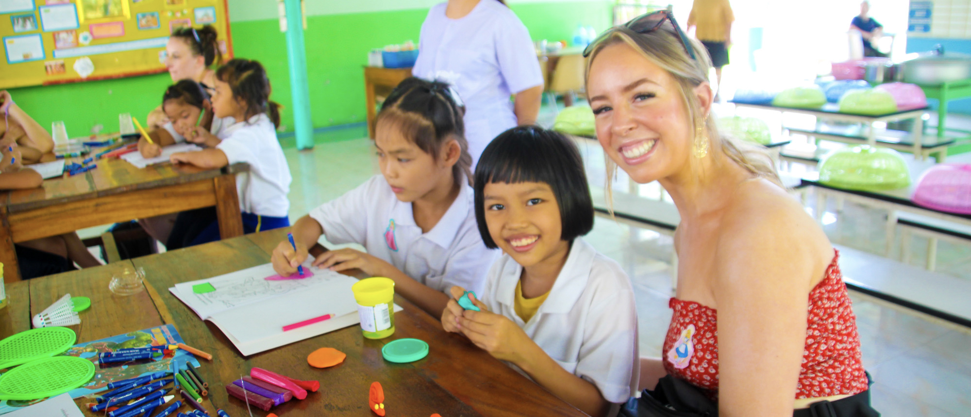 Backpacking travellers helping Thai students with schoolwork in a classroom