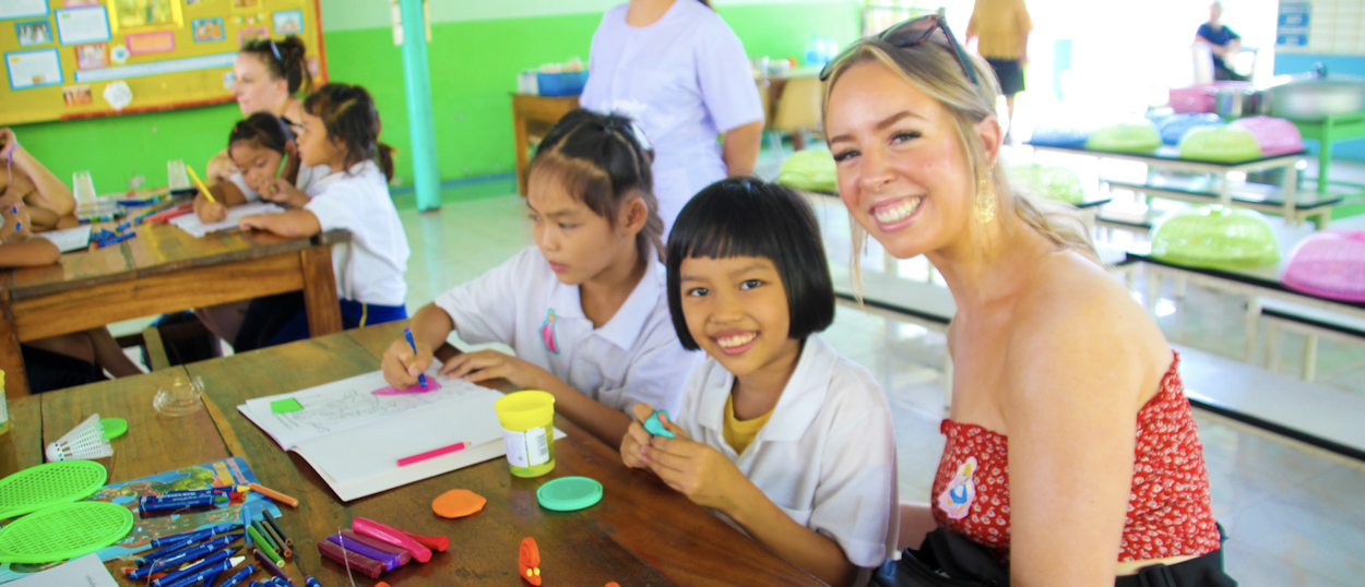 Backpacking travellers helping Thai students with schoolwork in a classroom