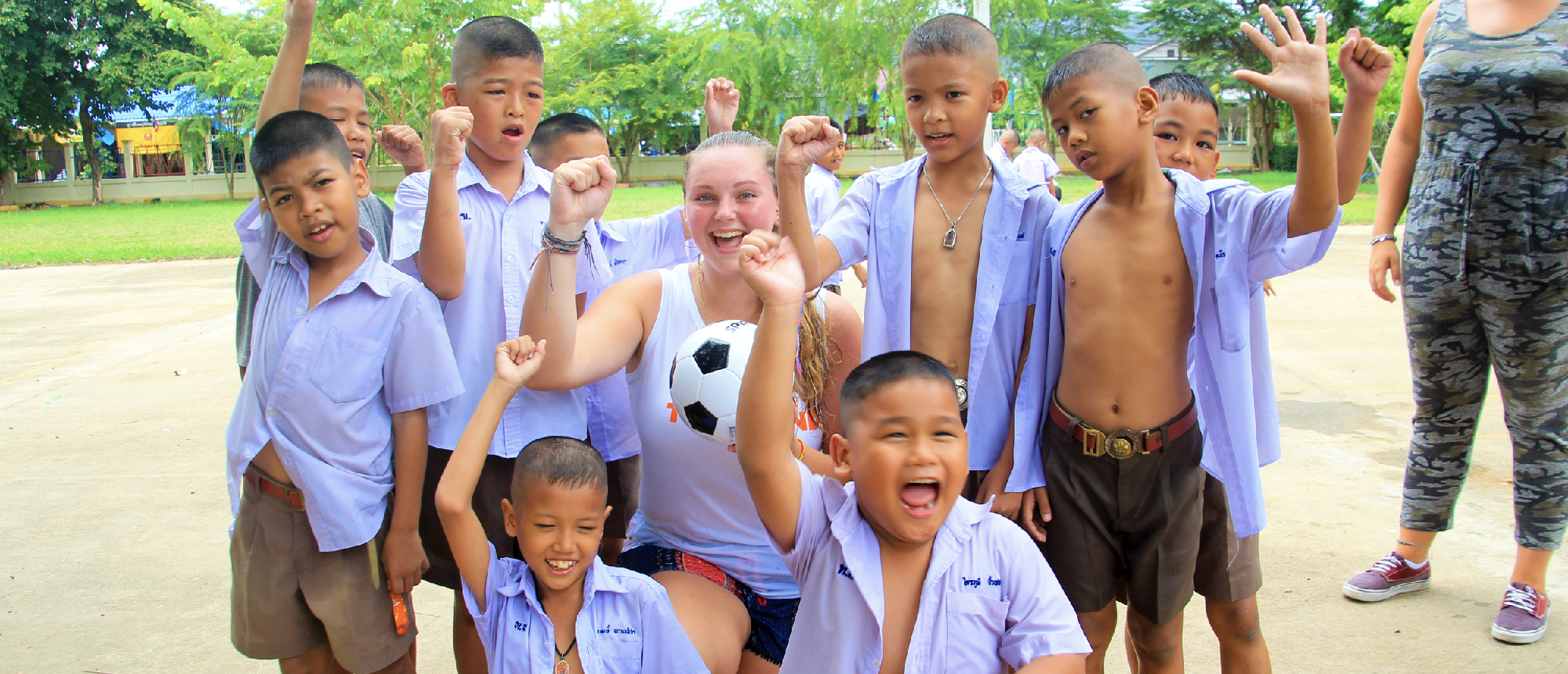 Backpacking group posing with smiling Thai schoolchildren at their school after class