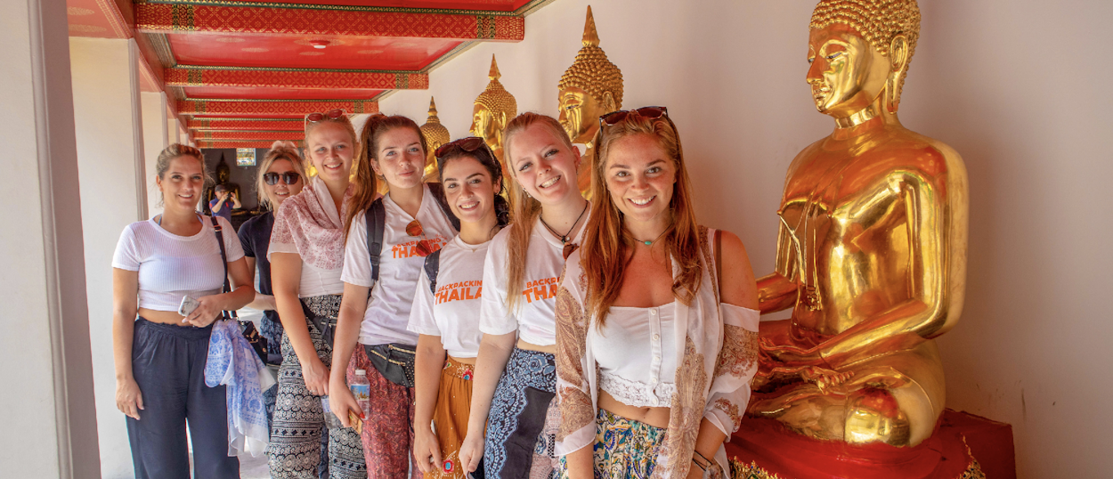 Backpacking group posing with a golden Buddha statue at Wat Pho temple