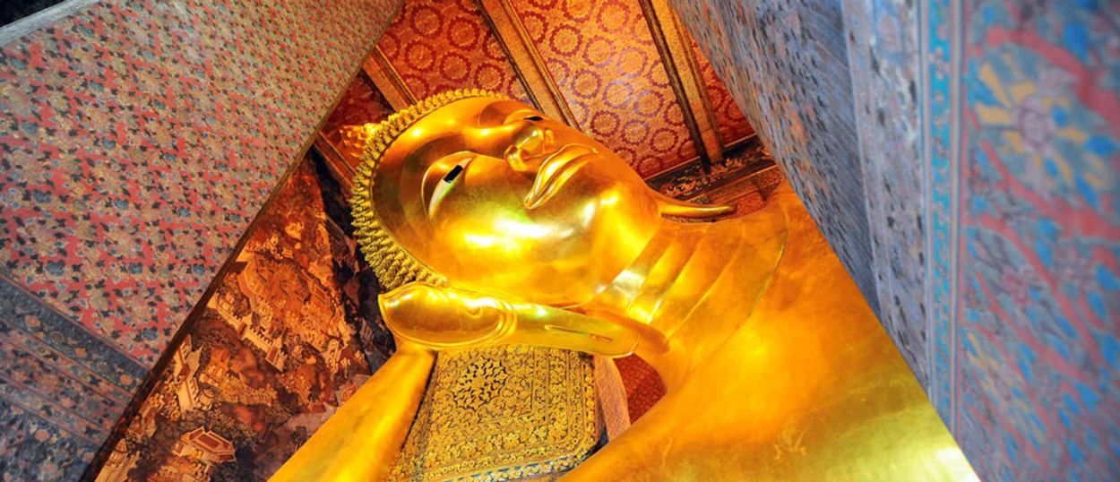 A massive golden reclining Buddha statue fills the frame, surrounded by ornate, colorful temple decorations in Bangkok.