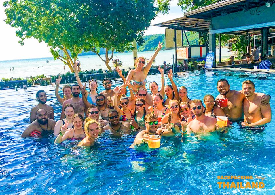 A large group of happy young travelers enjoying drinks in a sunny swimming pool in Thailand.