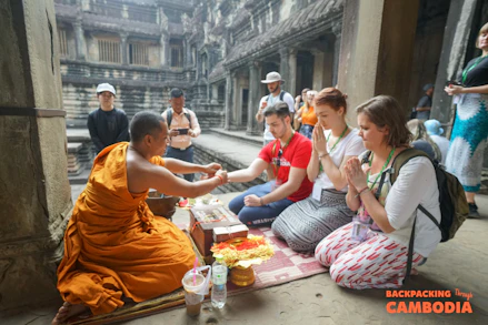 A Buddhist monk blesses three tourists kneeling inside the ancient stone temple of Angkor Wat.