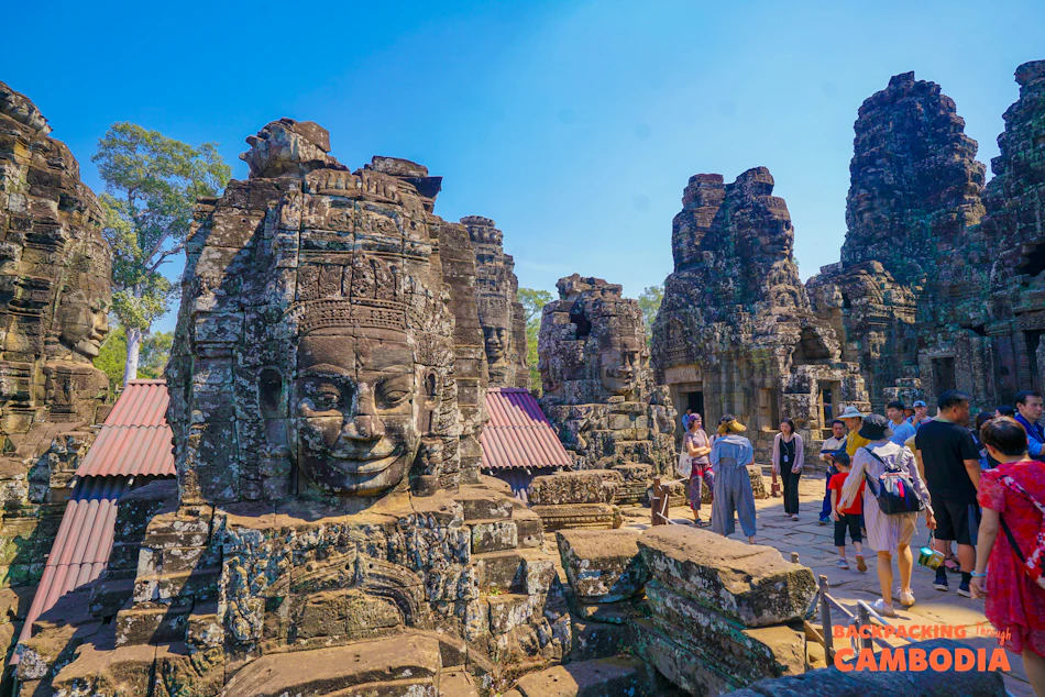 Tourists explore the ancient stone temple with giant carved faces at Bayon, Angkor Thom, Cambodia.