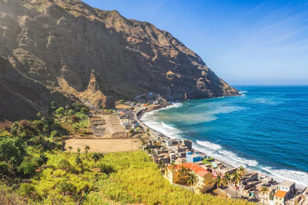A picturesque coastal village in Cape Verde nestled between a towering mountain and the blue ocean.