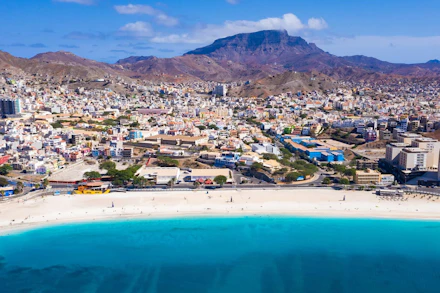 Vibrant Cape Verde coastal city with a white sand beach and turquoise ocean under blue sky.