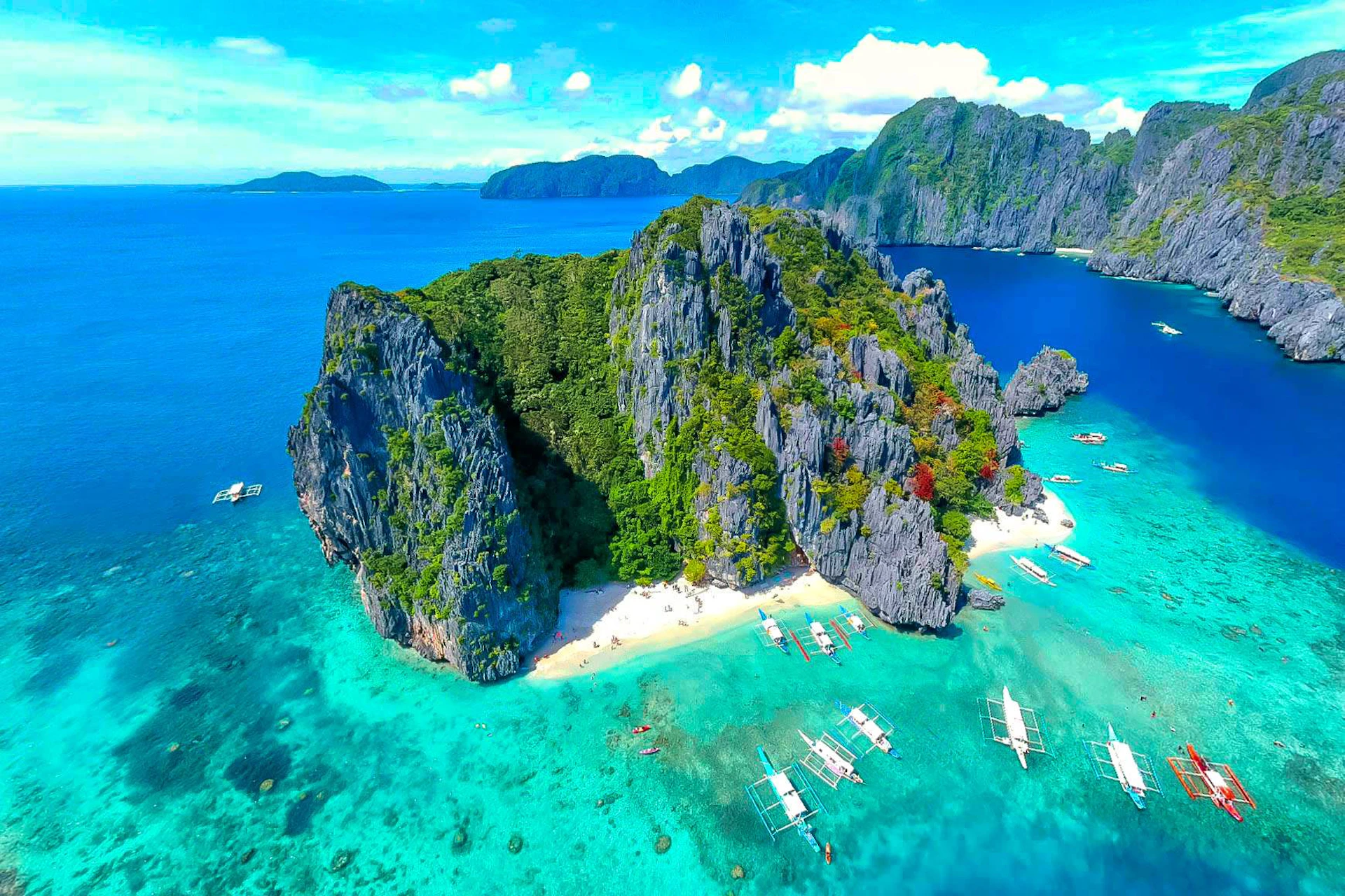 Tropical island with limestone cliffs, white sand beach, and boats in clear turquoise water, Palawan.