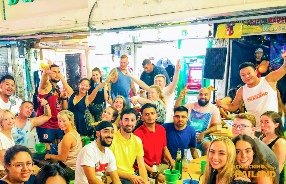A large group of happy backpackers enjoying drinks together in a lively Thai bar.
