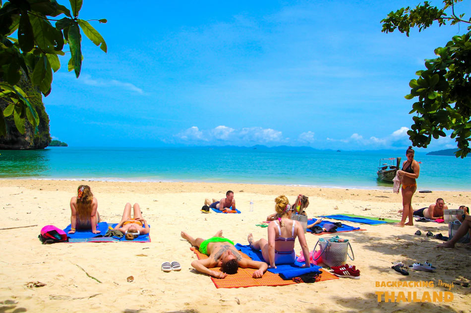 Tourists sunbathe on a beautiful sandy beach with clear blue water and distant islands in Thailand.