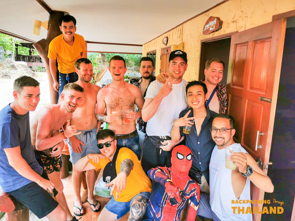 A group of happy men posing with drinks, one dressed as Spiderman, at a party in Thailand.