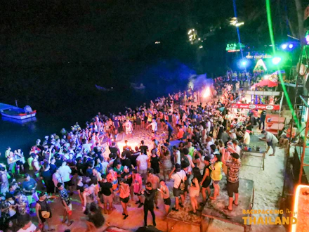 Energetic full moon party in Thailand with a large crowd dancing on the beach at night.