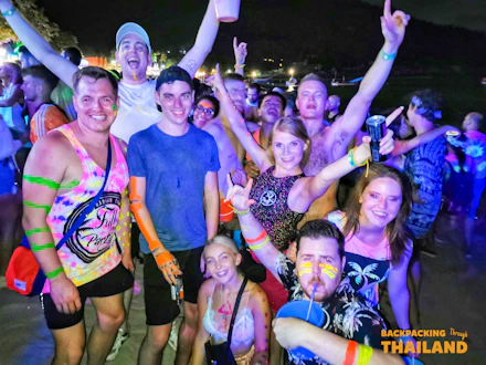 Smiling friends with neon paint celebrating on a beach during a vibrant Full Moon Party.