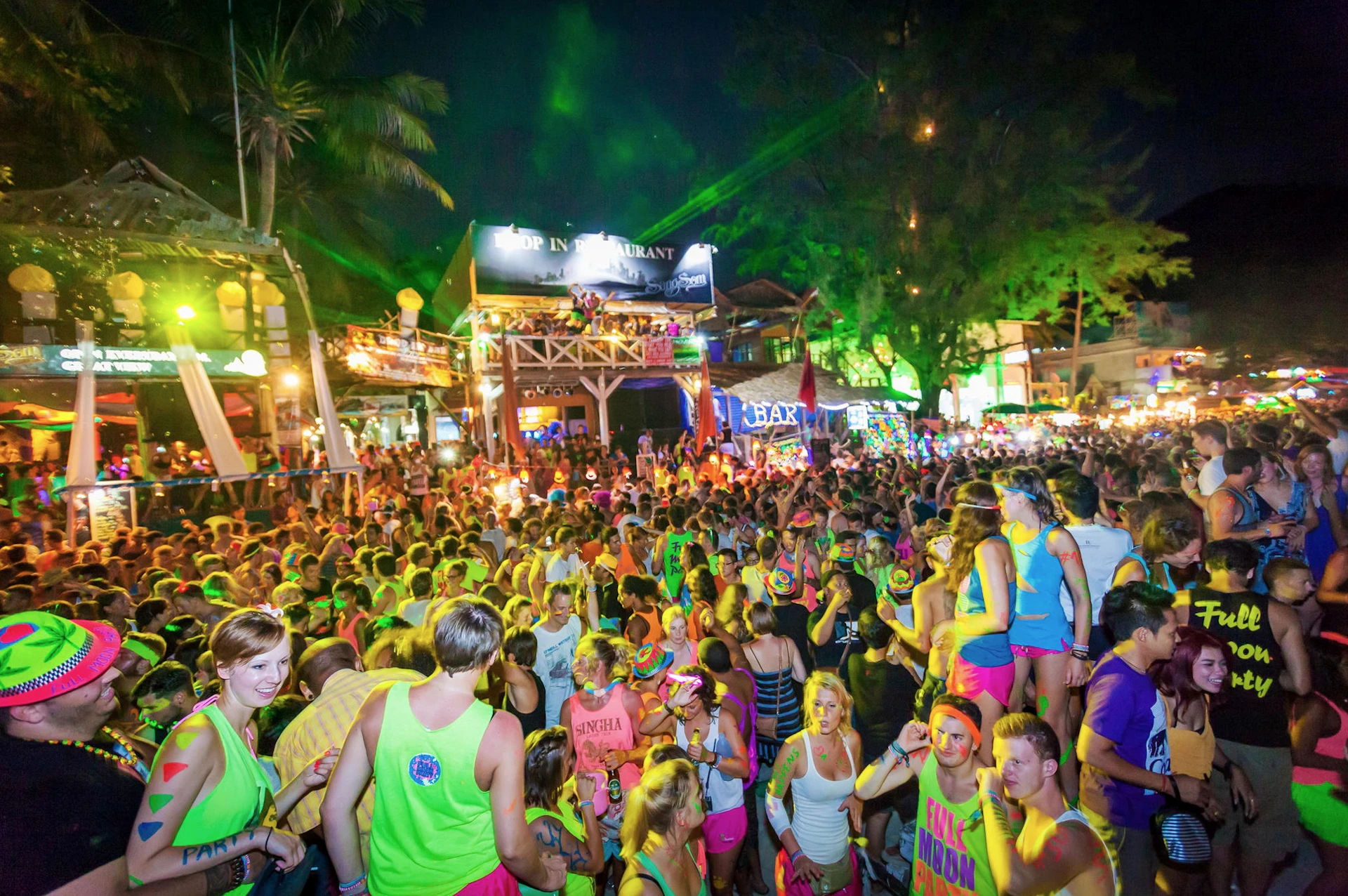 Thousands of partygoers dancing on a beach at night during the Full Moon Party in Thailand.
