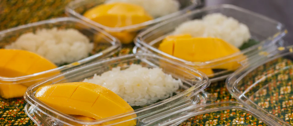 Fresh mango sticky rice desserts in plastic containers, ready for street food enjoyment in Thailand.