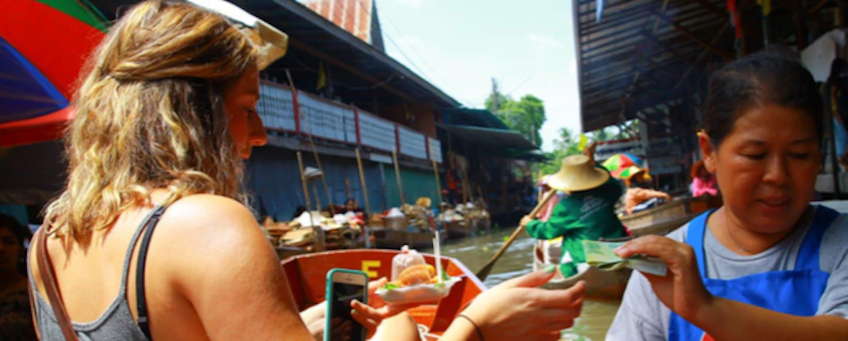 A traveler pays a local vendor from her boat at a busy floating market in Thailand.