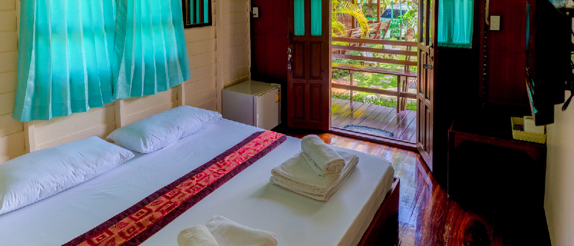 Traditional Thai homestay room with a double bed and colourful bedspread overlooking the river