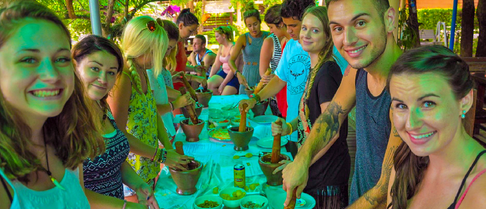 Backpacking group enjoying a Thai cooking lesson with local hosts after visiting a school