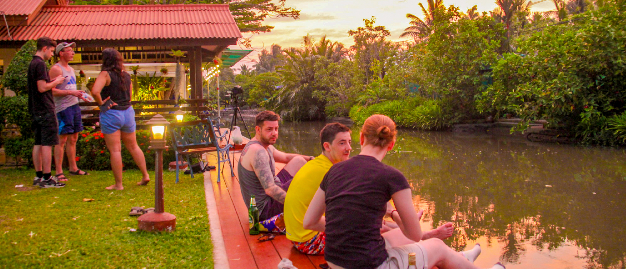 Backpacking group enjoying dinner at an outdoor long table by the river during their homestay