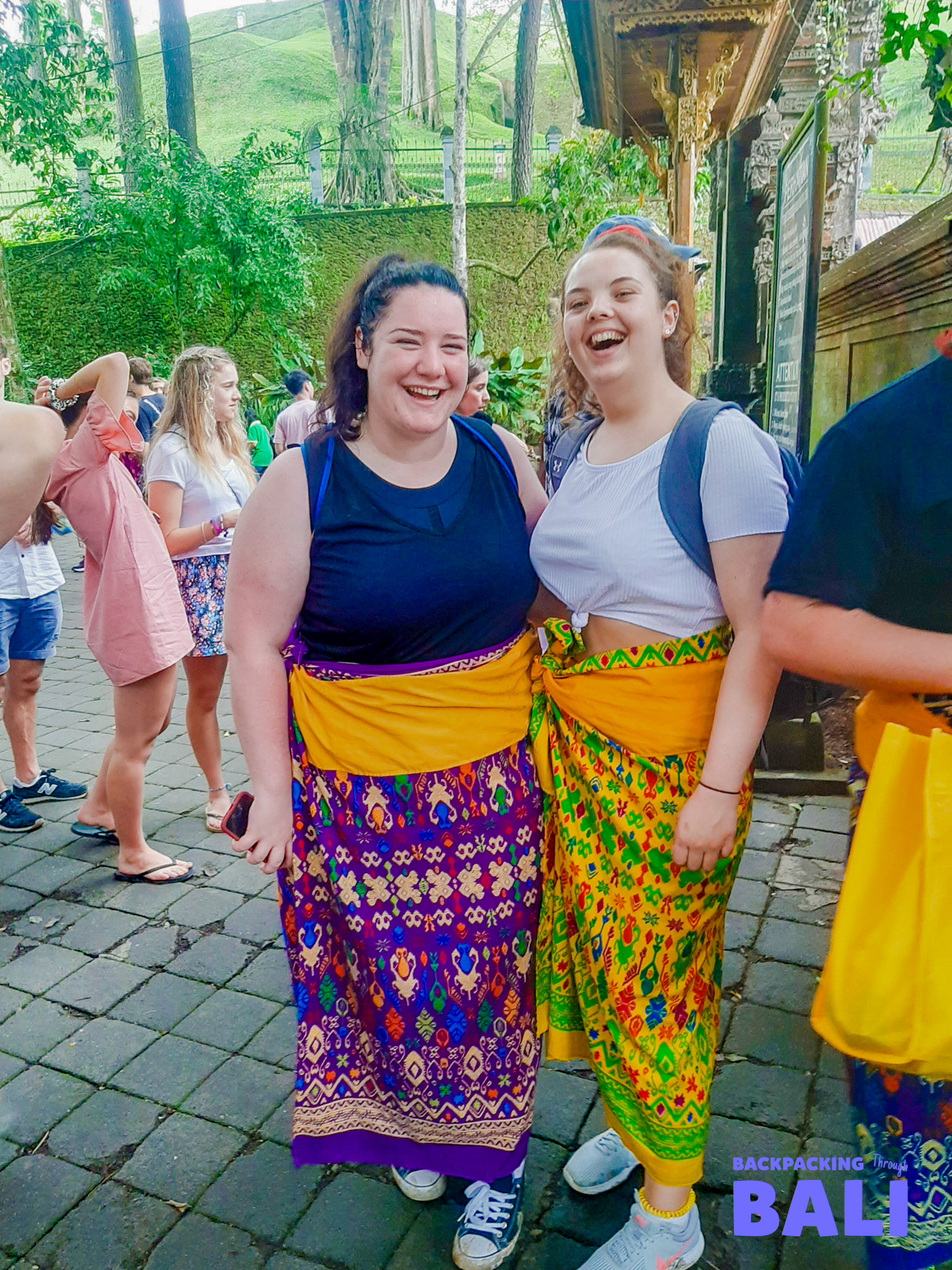 Two female travellers wearing sarongs smiling at a Balinese temple