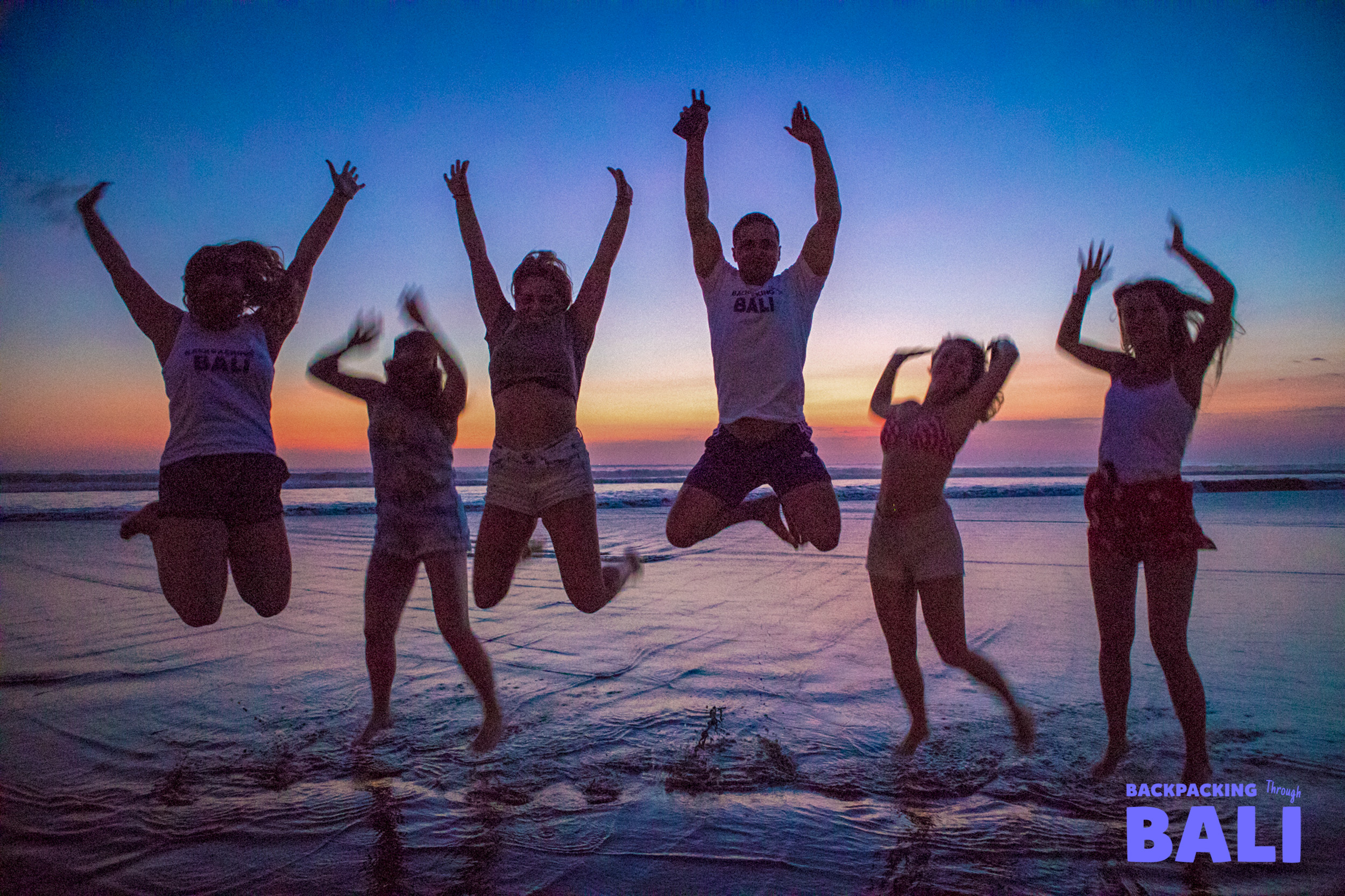 Backpacking group jumping on the beach at sunset
