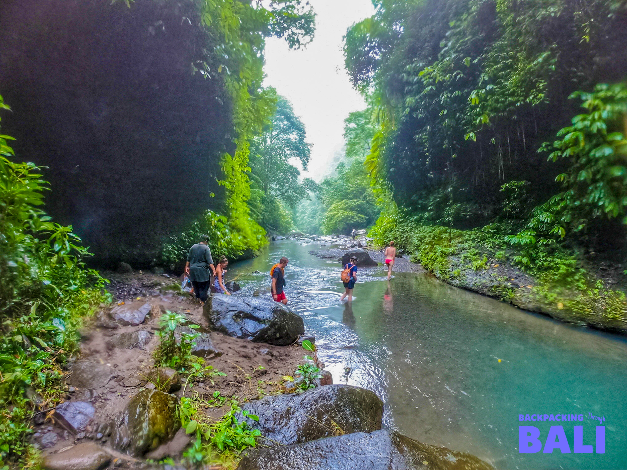 Backpacking group walking across a shallow stream in the jungle