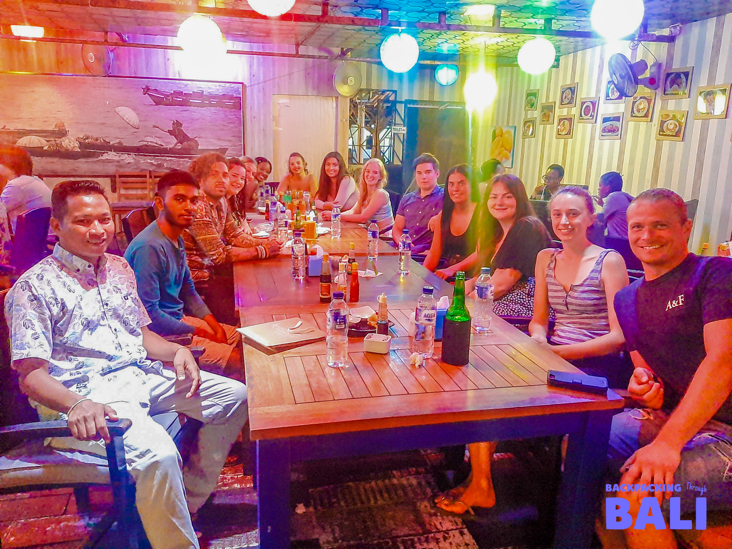 Backpacking group enjoying dinner and drinks at a lively bar with colourful lights