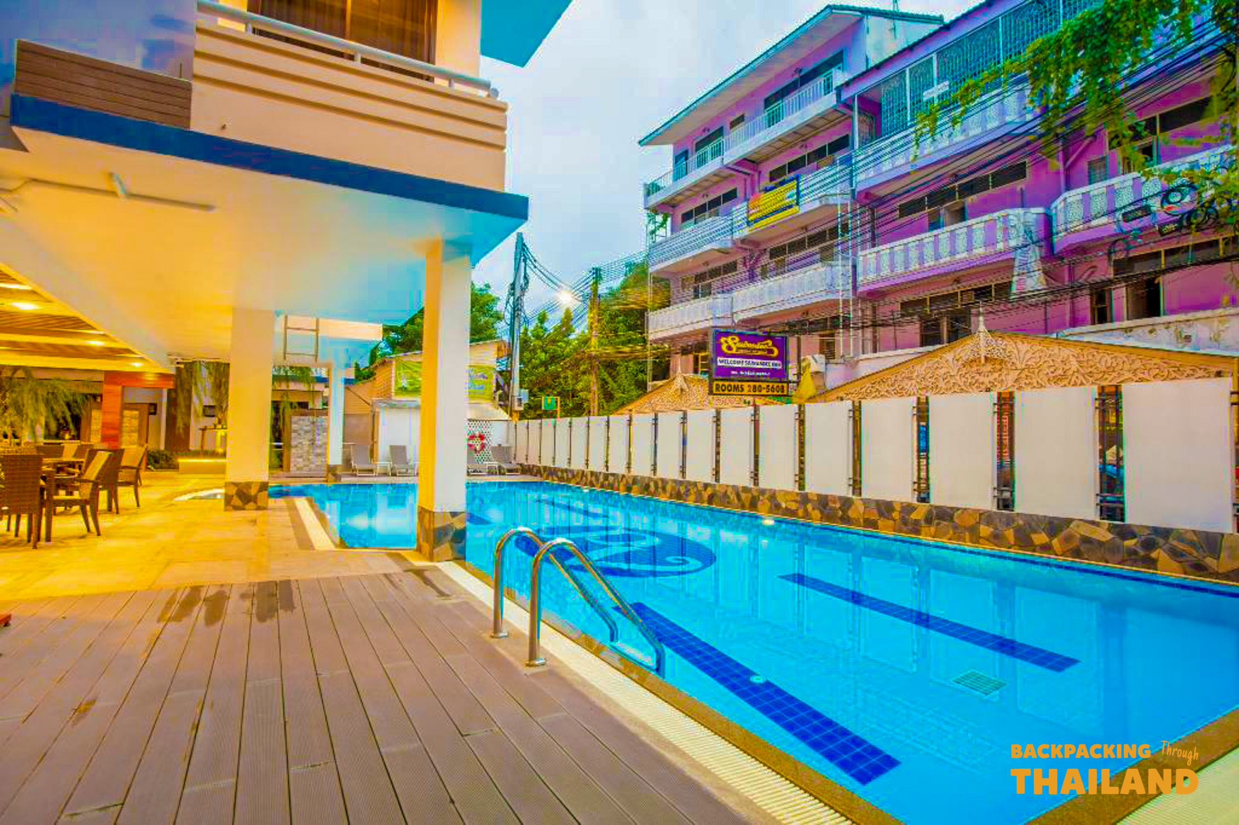 Wooden deck walkway next to a long swimming pool with colorful balconies in Bangkok