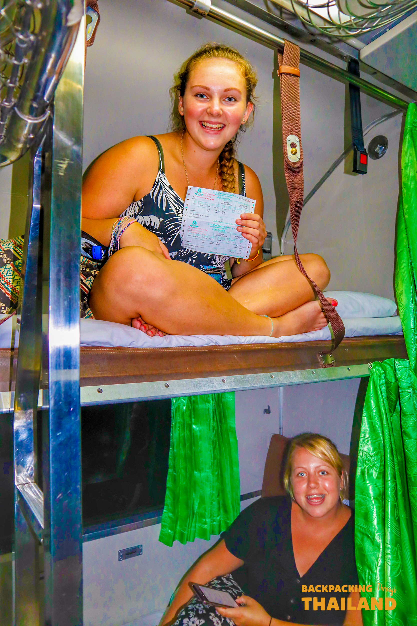 Backpacking travellers sitting on top and bottom bunk beds in an overnight train with green curtains